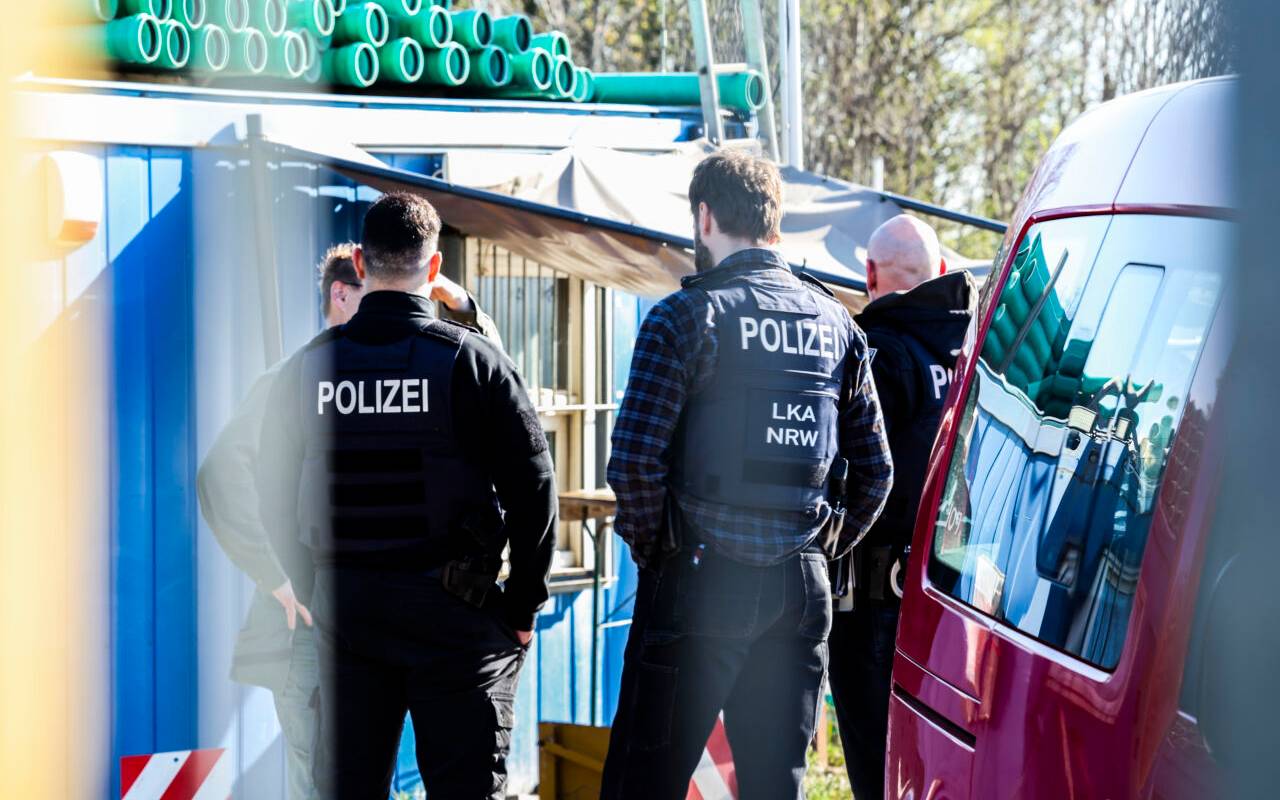 Polizeibeamte und LKA-Mitarbeiter stehen auf dem Betriebsgelände einer Kiesgrube.