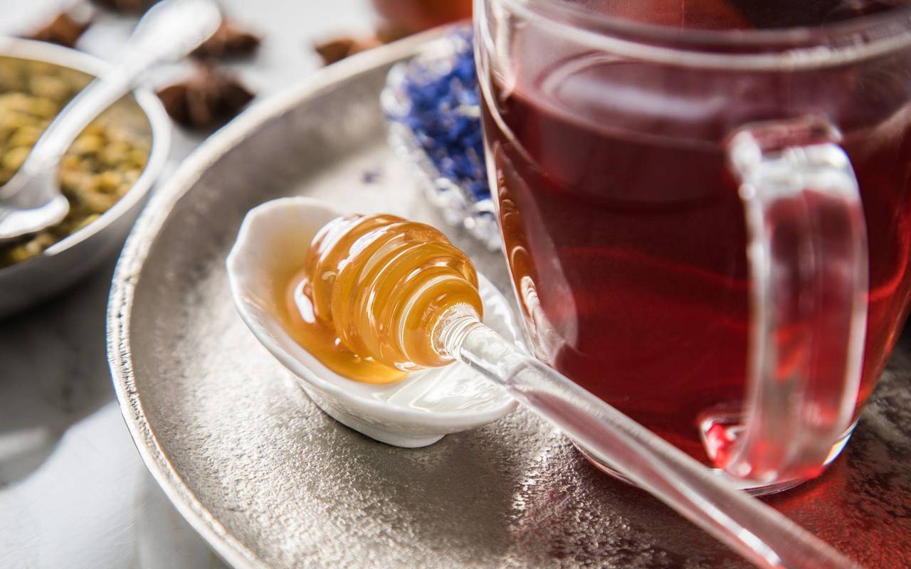 Ein Honiglöffel mit Waldhonig liegt neben einer Tasse Tee