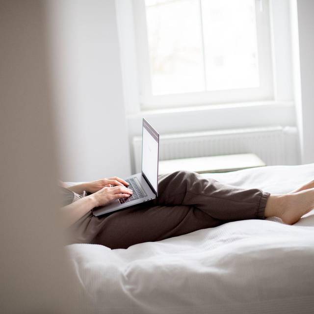 Eine Frau sitzt mit Laptop im Bett