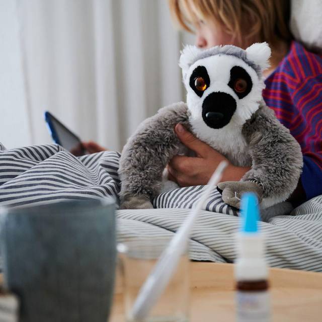 Krankes Kind liegt mit einem Kuscheltier im Bett