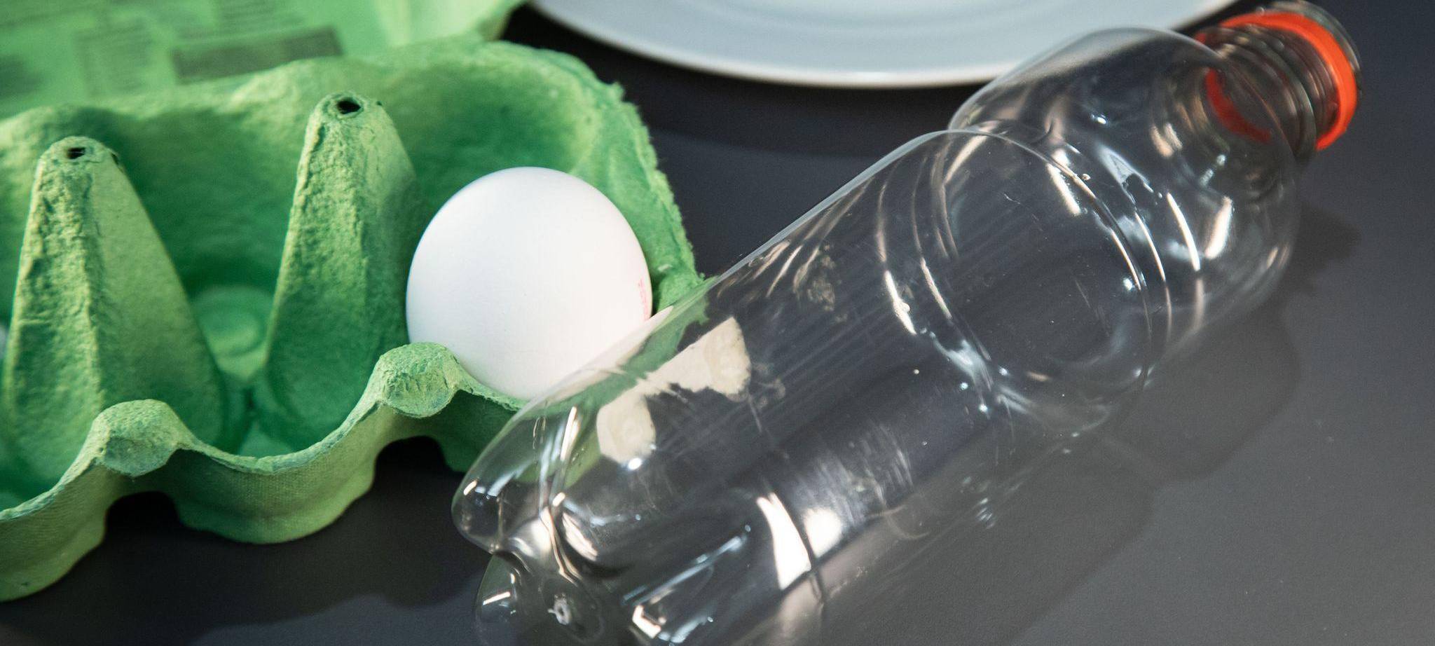 Ein Ei liegt neben einer Plastikflasche