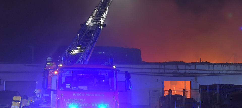 Feuerwehrwagen mit Drehleiter löscht brennendes Gebäude