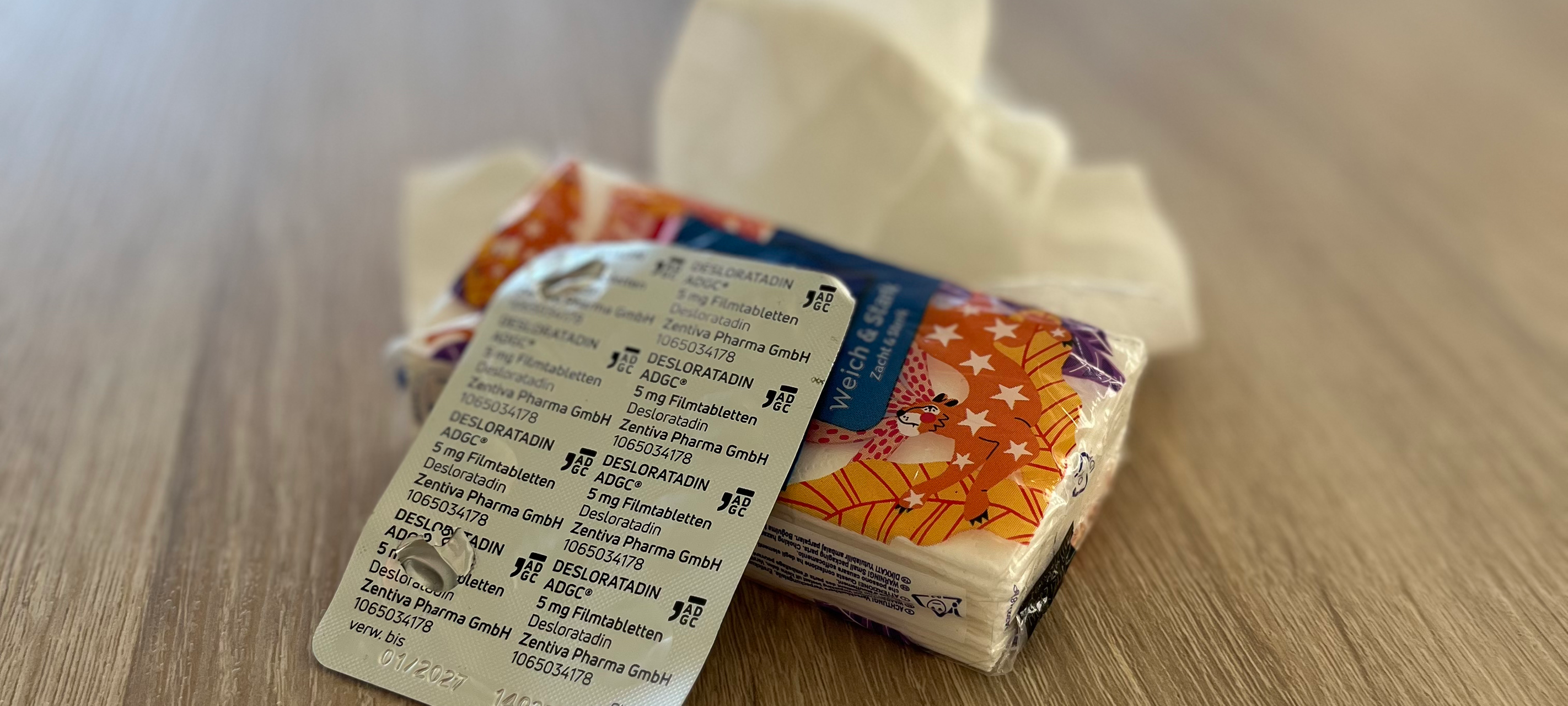 Eine Packung Taschentücher, ein Blister mit Allergietabletten und im Hintergrund ein benutztes Taschentuch.